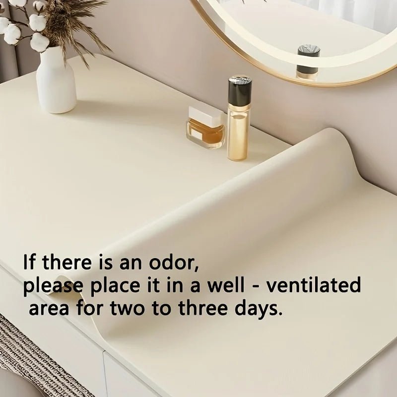 Cream-colored desk mat on a white table with skincare products and a vase of flowers.