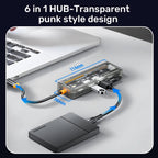Transparent 6-in-1 USB-C hub with punk style design connected to a laptop and external drive.